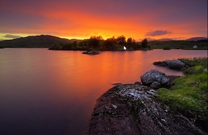 A calm lake with a sunset, surrounded by hills and a small island. - Screebe House (Derravonniff)