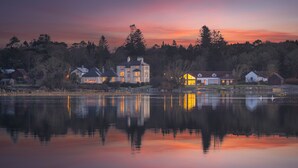 Une propriété au bord du lac comprenant plusieurs maisons, un grand bâtiment central avec des fenêtres illuminées, et une étendue d’eau calme qui reflète les bâtiments.