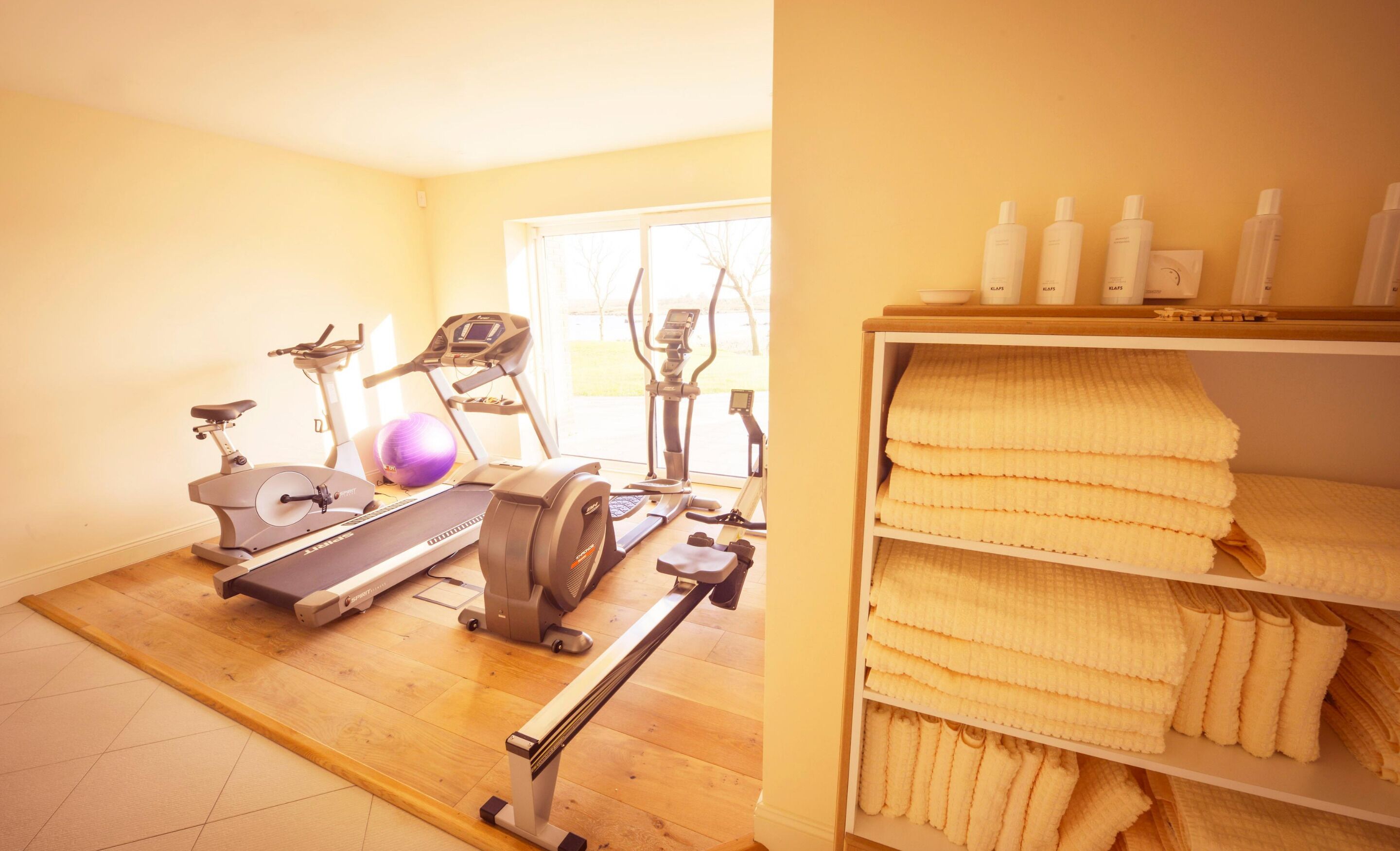 Une salle de sport à domicile équipée de matériel d’exercice, d’un tapis de yoga et d’une étagère avec des serviettes.