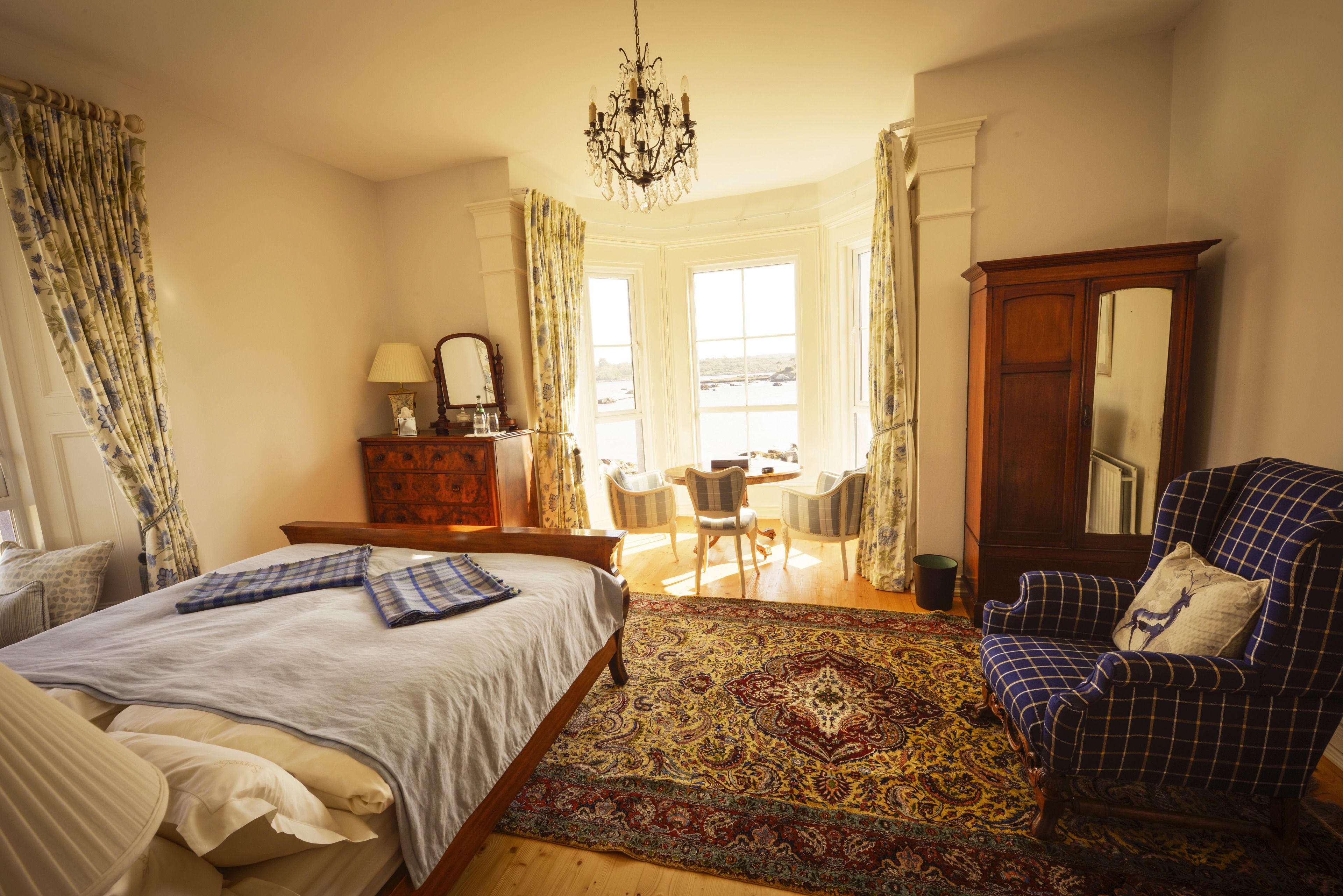 Ein Schlafzimmer mit einem großen Bett, einem Holzschrank, einem blauen Sessel und einem gemusterten Teppich.