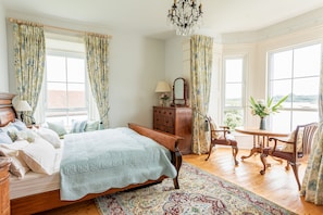 A bedroom with a wooden bed, a dresser, a chair, a table, and a chandelier. - Screebe House (Derravonniff)