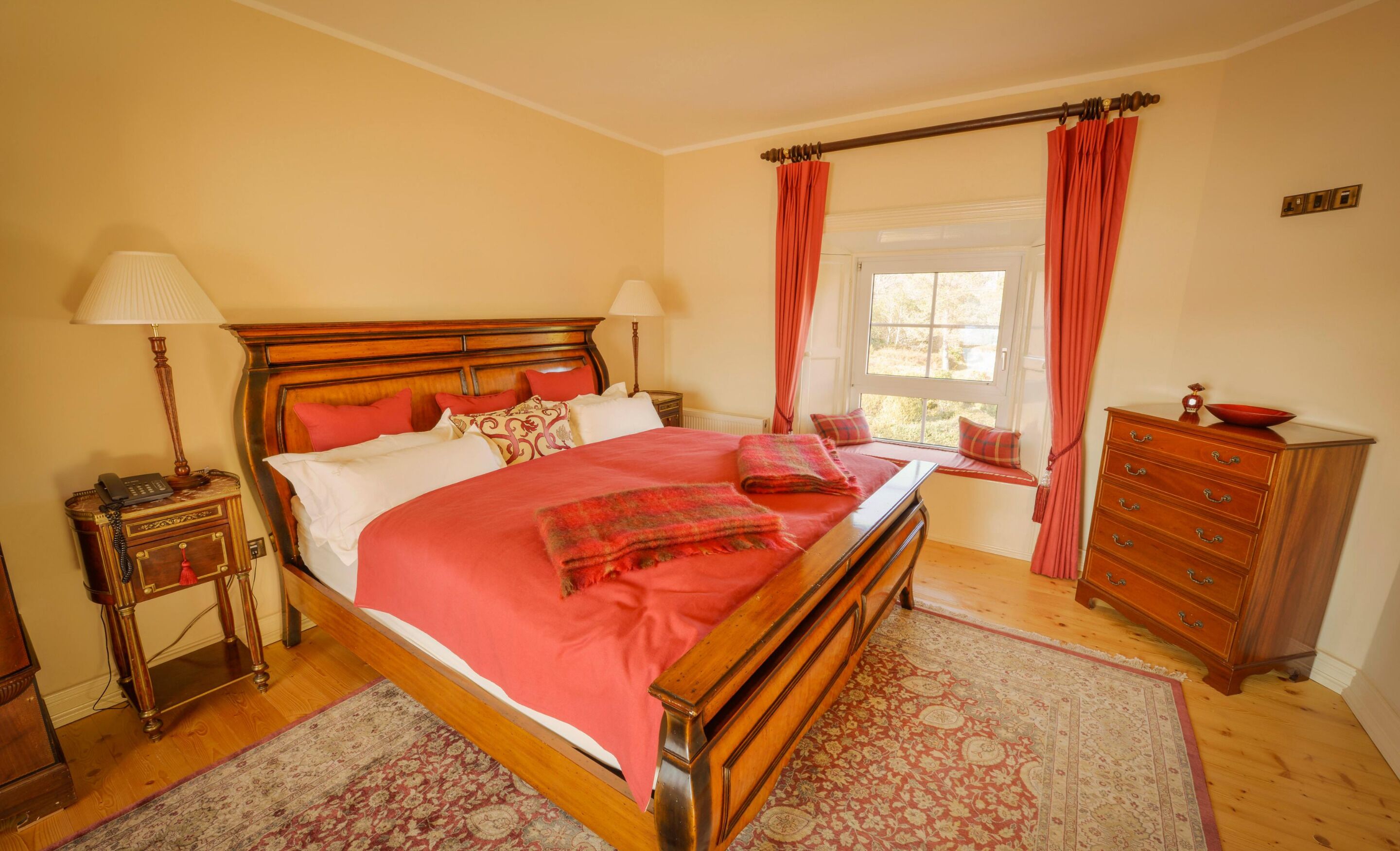 A bedroom with a wooden bed, two bedside tables, a dresser, and a window with curtains.