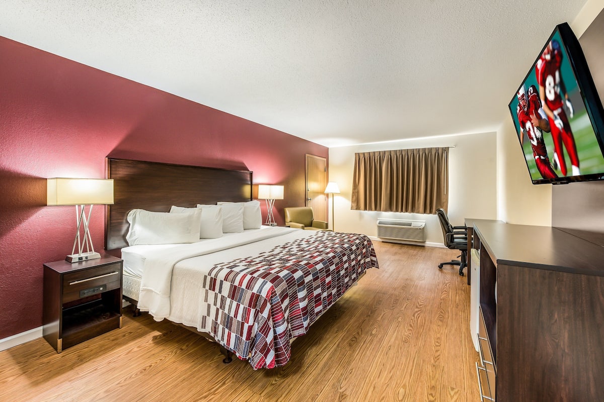 Een hotelkamer met een groot bed, twee nachtkastjes, een bureau, een flatscreen televisie en een raam met gordijnen.