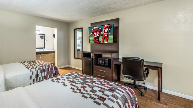 A hotel room with two beds, a desk, a television, and a mirror. - Red Roof Inn & Suites Wapakoneta (Wapakoneta)