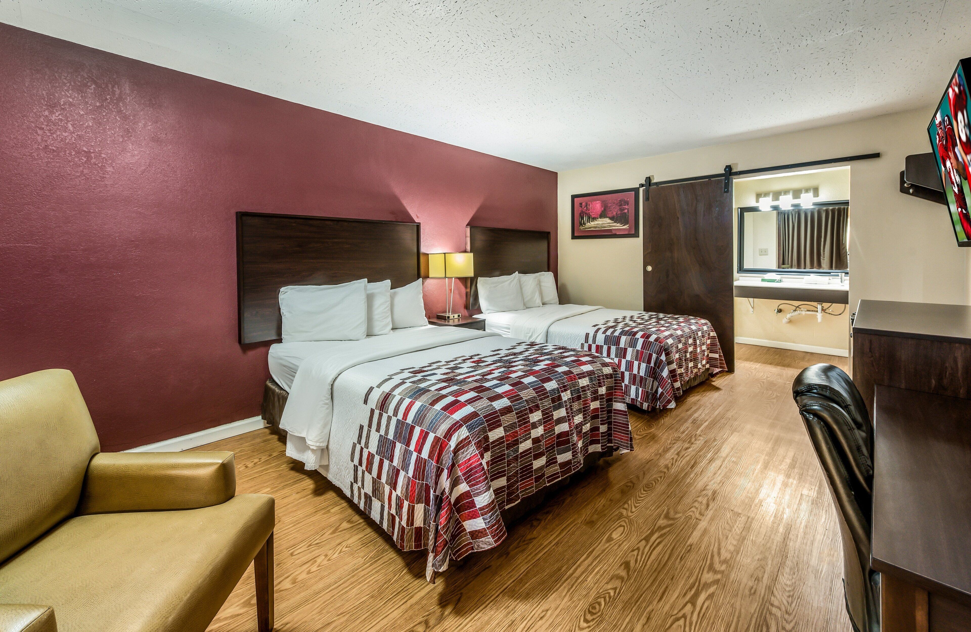 A hotel room with two beds, a desk, a chair, and a TV.