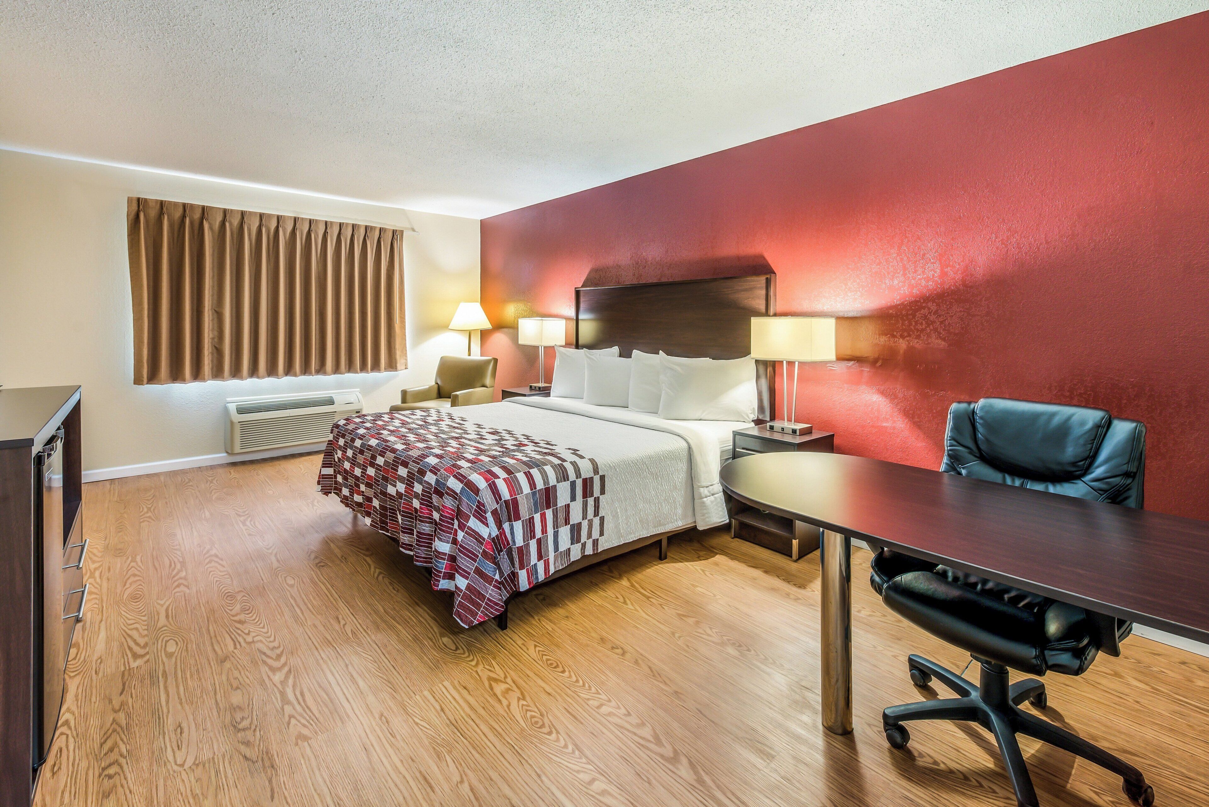 Una habitación de hotel con cama, mesitas de noche, escritorio, silla y ventana con cortinas.