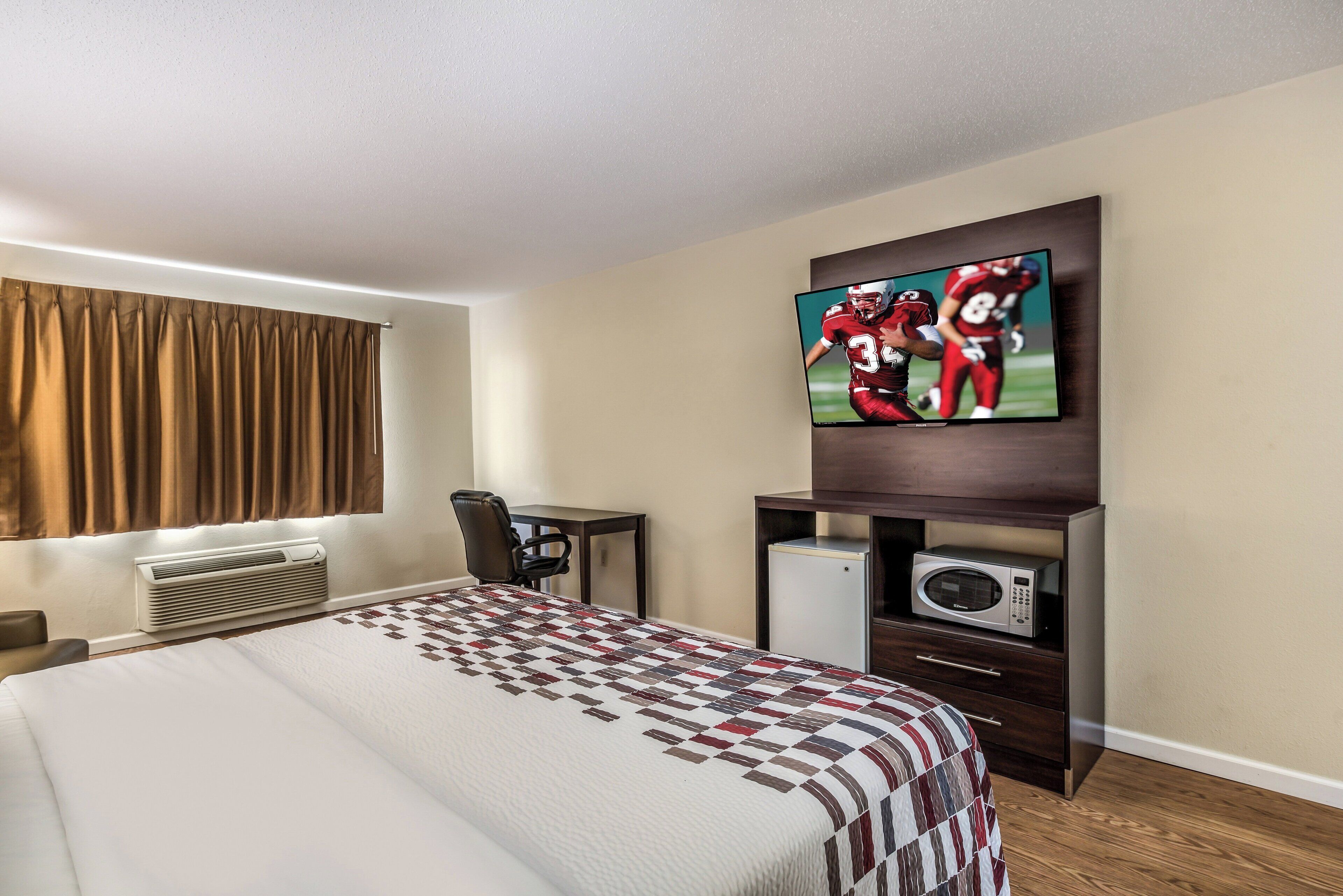 A hotel room with a bed, a desk, a television, an air conditioner, and a microwave.