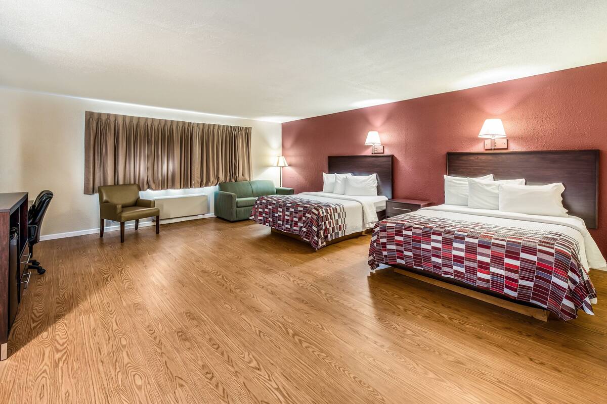 Ein Hotelzimmer mit zwei Betten, einem Schreibtisch, einem Stuhl und einem Vorhangfenster.