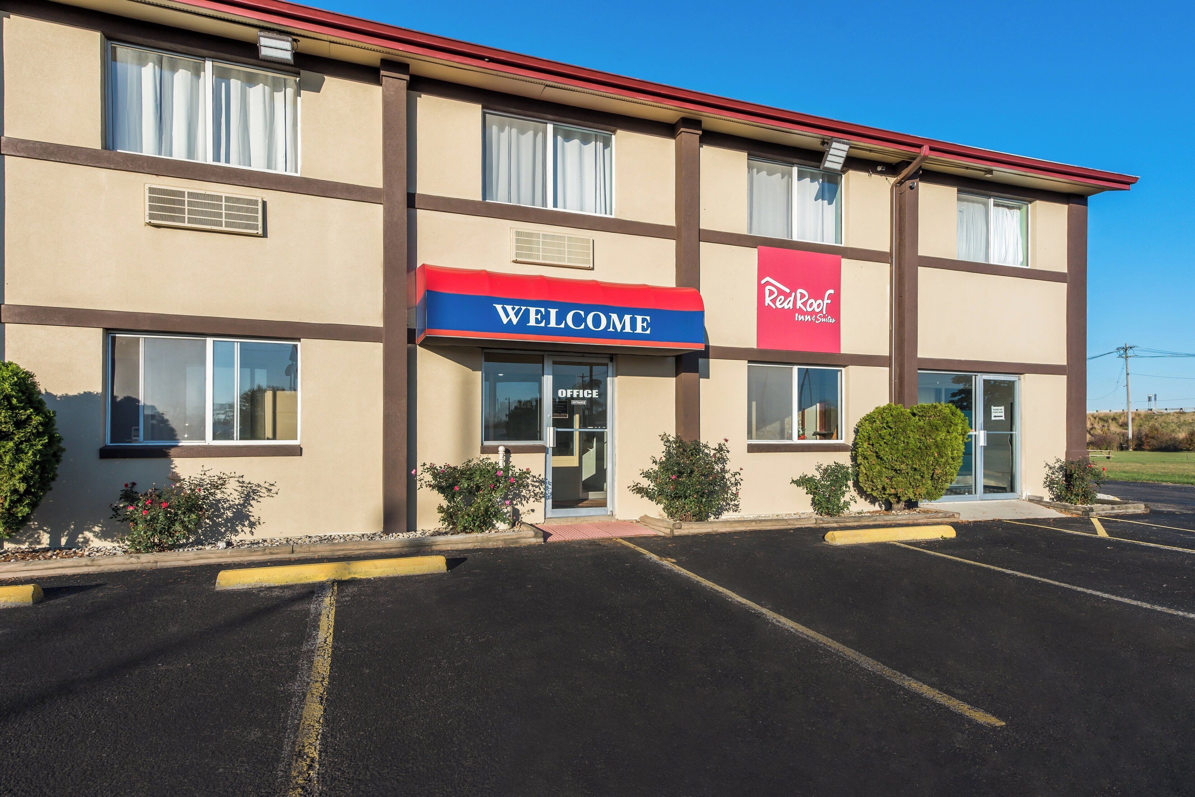 Un Red Roof Inn & Suites con un cartel que dice 'Welcome', un estacionamiento y cielo despejado.