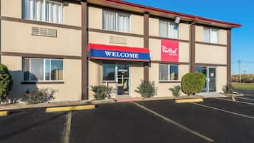 Un Red Roof Inn & Suites con un cartel que dice 'Welcome', un estacionamiento y cielo despejado.
