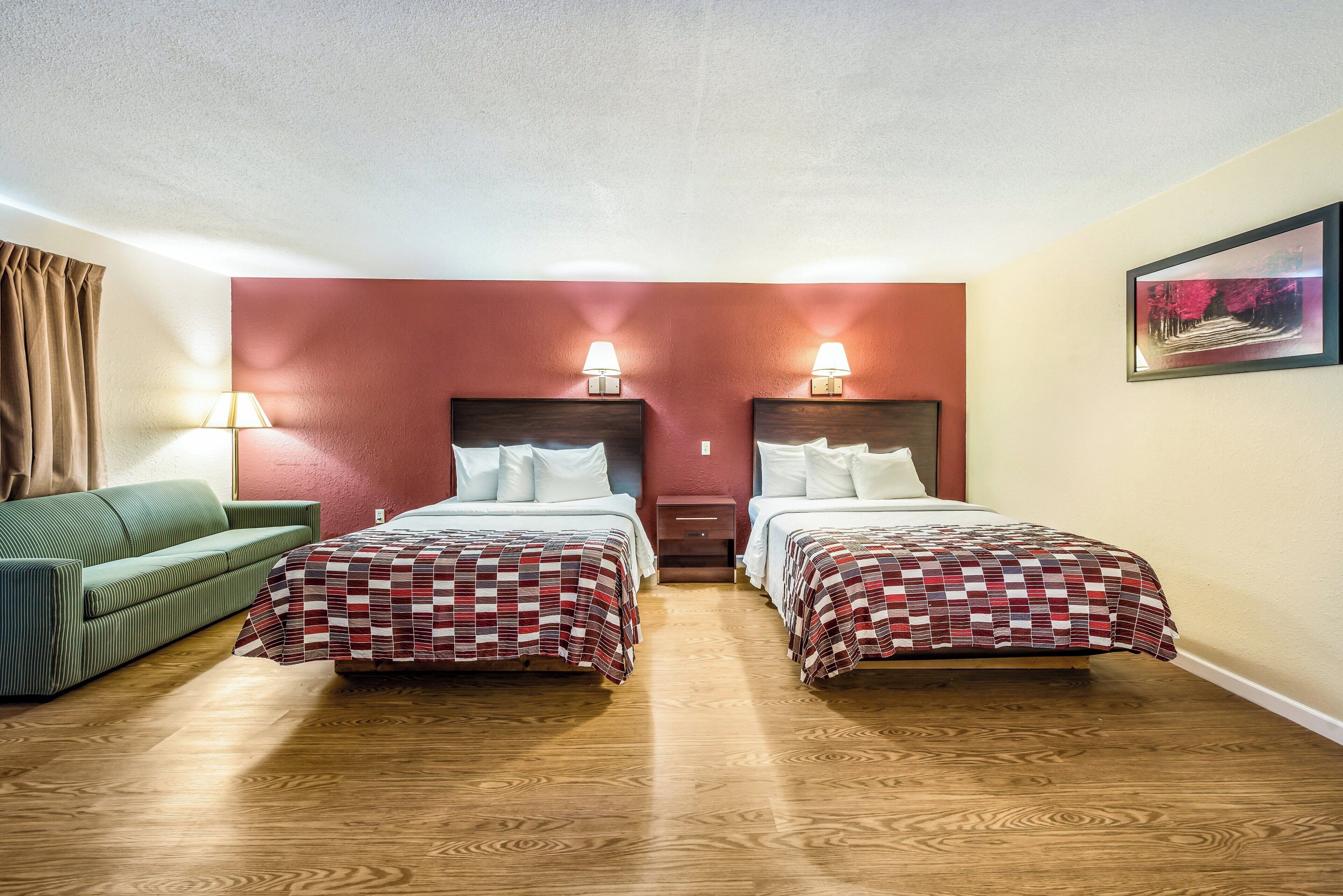 A hotel room with two beds, a green sofa, wooden flooring, and a painting on the wall.