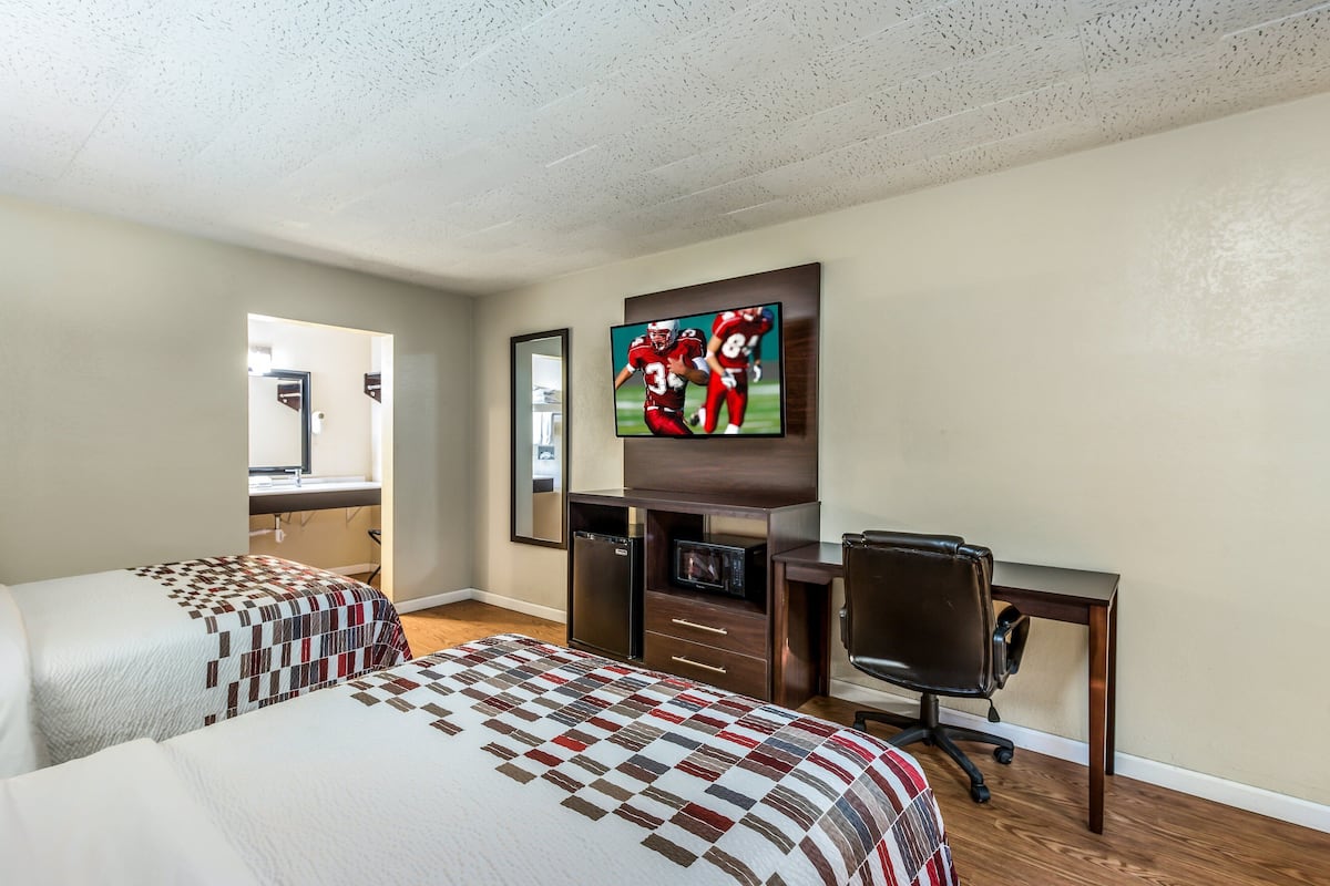 Een hotelkamer met twee bedden, een bureau, een stoel, een televisie en een spiegel.