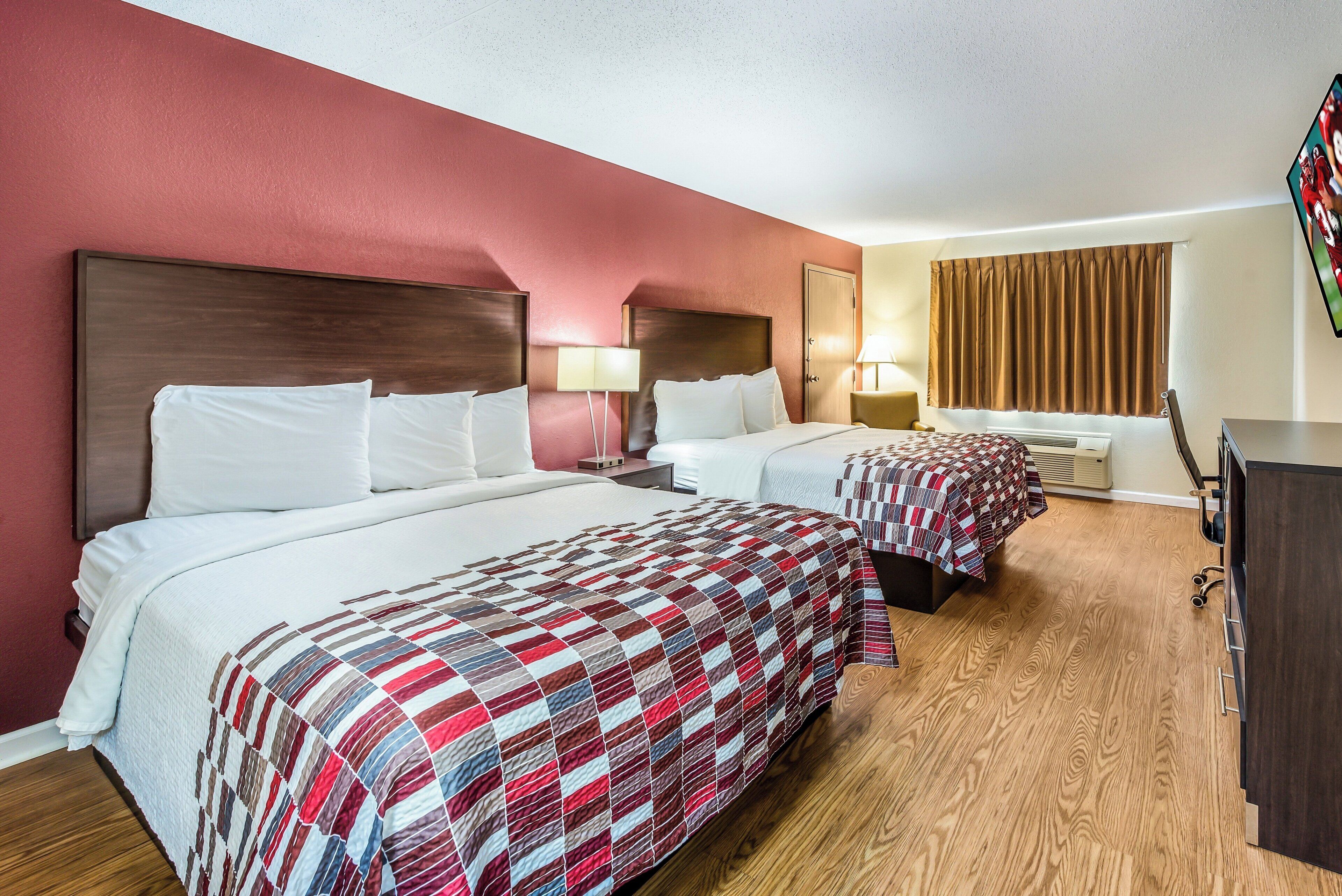 Een hotelkamer met twee bedden, een houten vloer en een aan de muur bevestigde televisie.