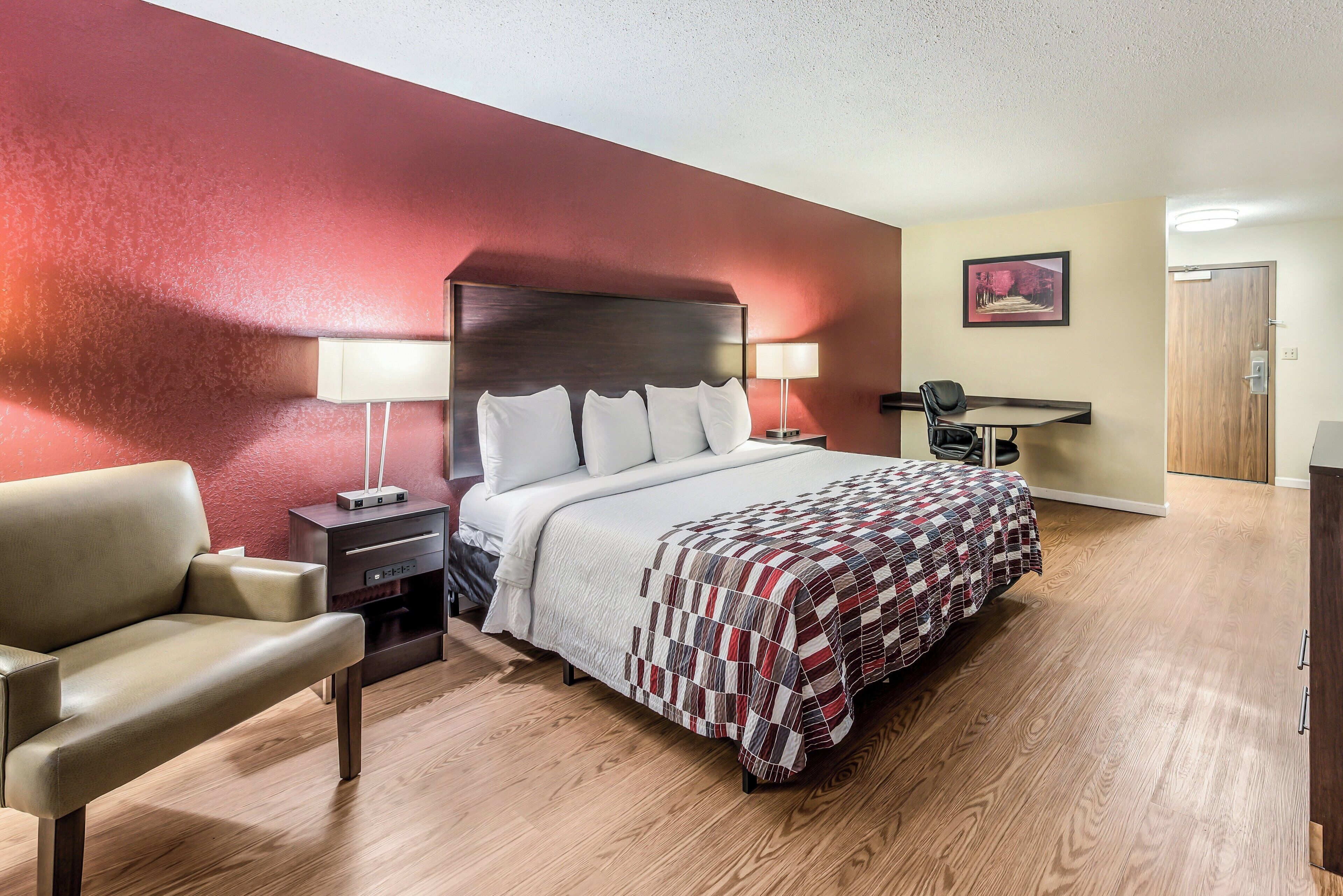 A hotel room with a bed, bedside tables, a desk, a chair, and a door.