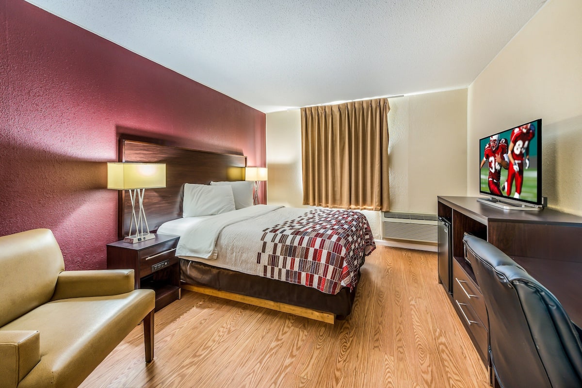 Een hotelkamer met een bed, een bureau, een televisie, een stoel en een lamp.