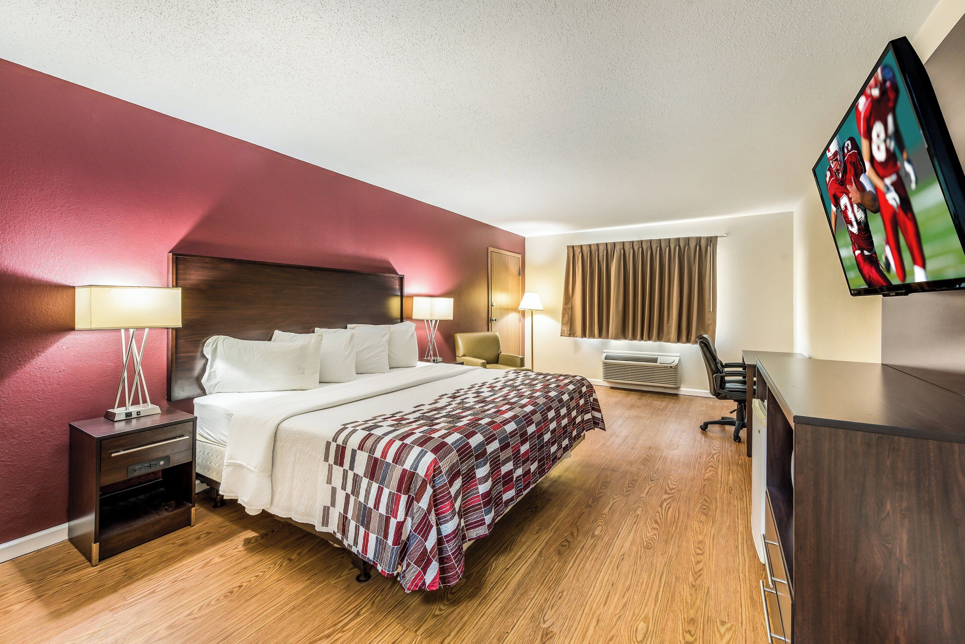 A hotel room with a bed, bedside tables, a desk, a chair, a TV, and a window with curtains.
