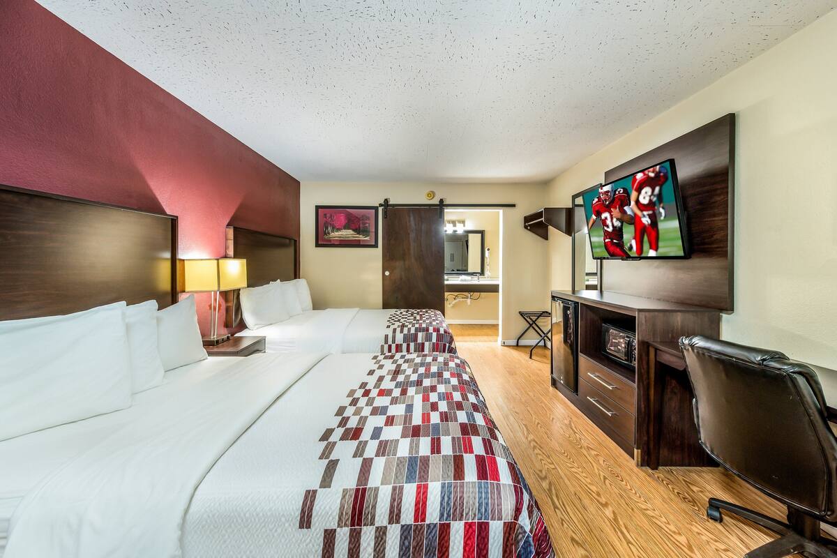 Ein Hotelzimmer mit einem großen Bett, einem Schreibtisch mit Stuhl, einem Fernseher und einem Spiegel.