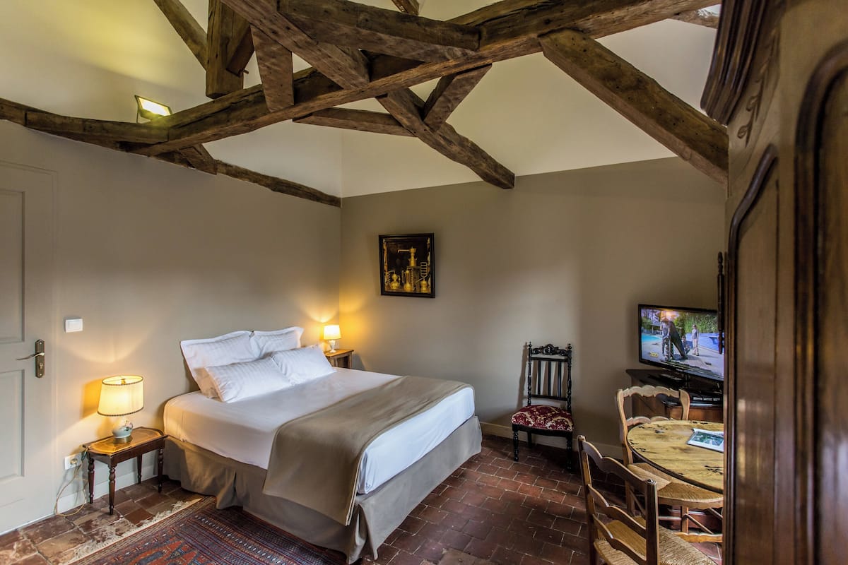 A bedroom with a bed, bedside lamps, a television, and a dining table with chairs.