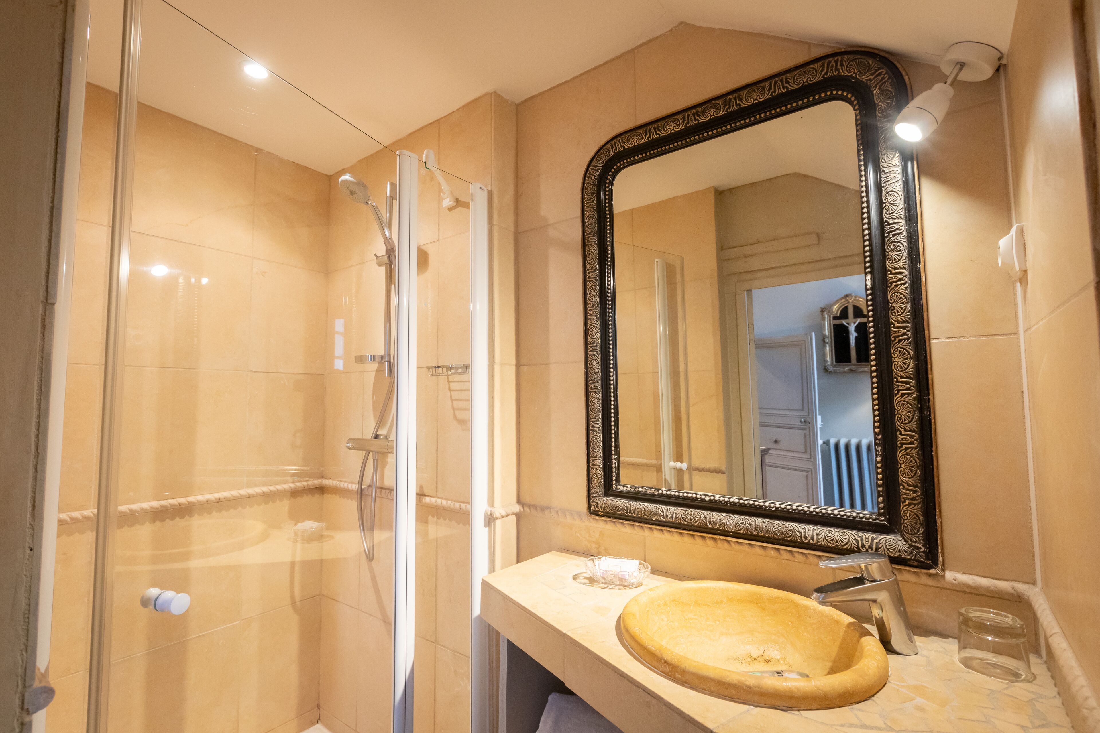 Une salle de bain dotée d’une douche à parois de verre, d’un lavabo rond et d’un grand miroir décoratif.