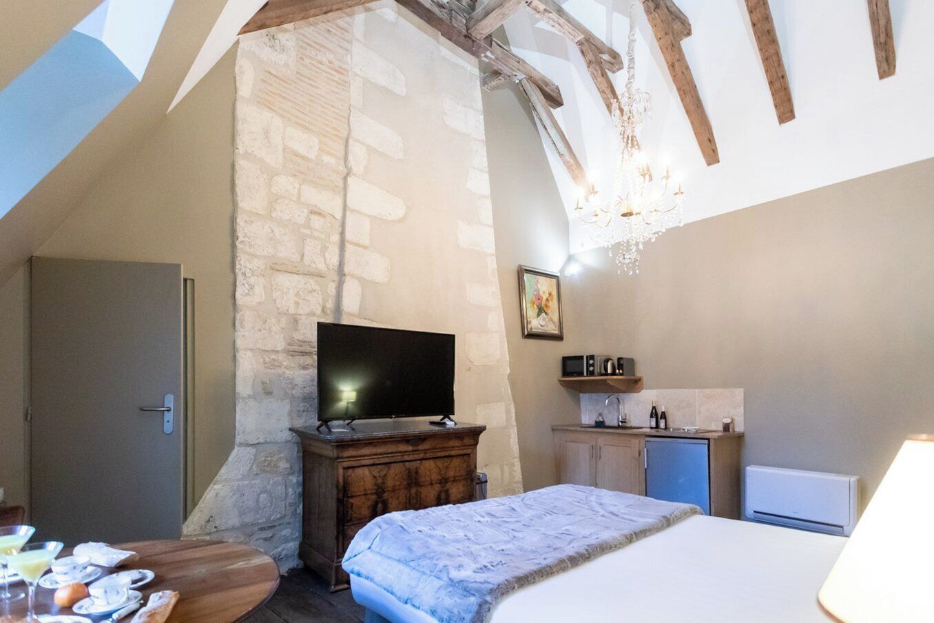 A bedroom with a stone wall, a wooden bed, a TV, a small kitchen area with a microwave, and a door.