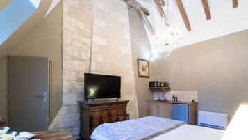 A bedroom with a stone wall, a wooden bed, a TV, a small kitchen area with a microwave, and a door.