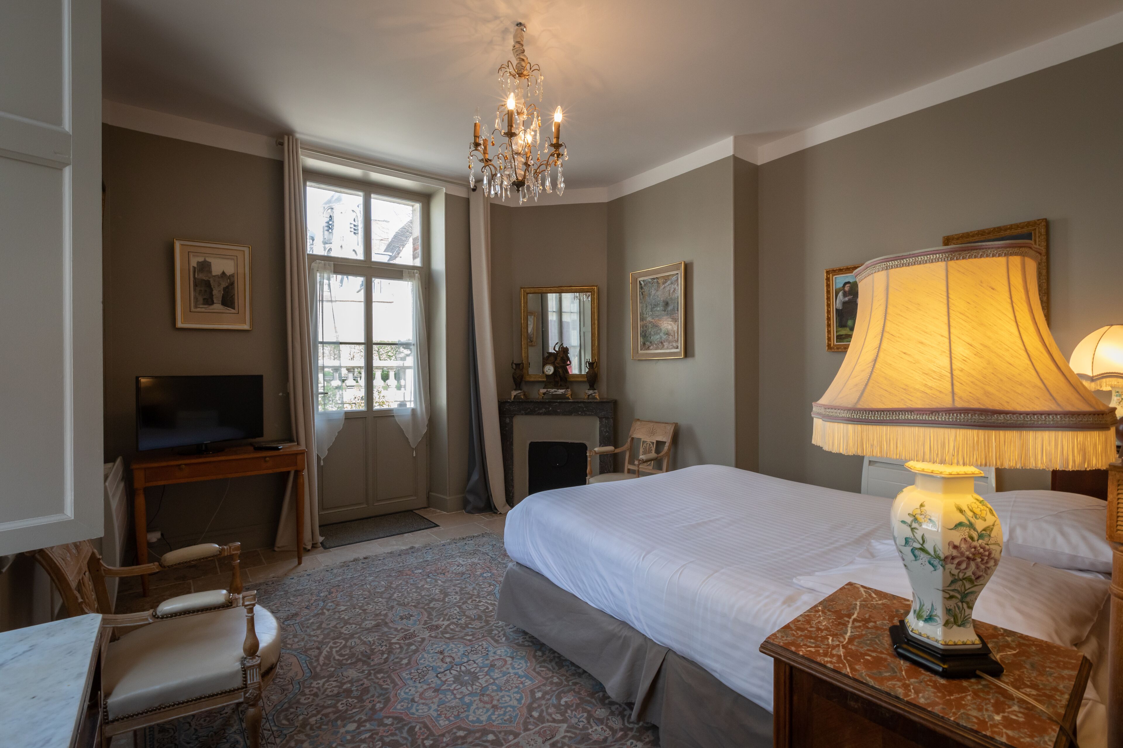 A hotel room with a large bed, a television, a fireplace, and a chandelier.