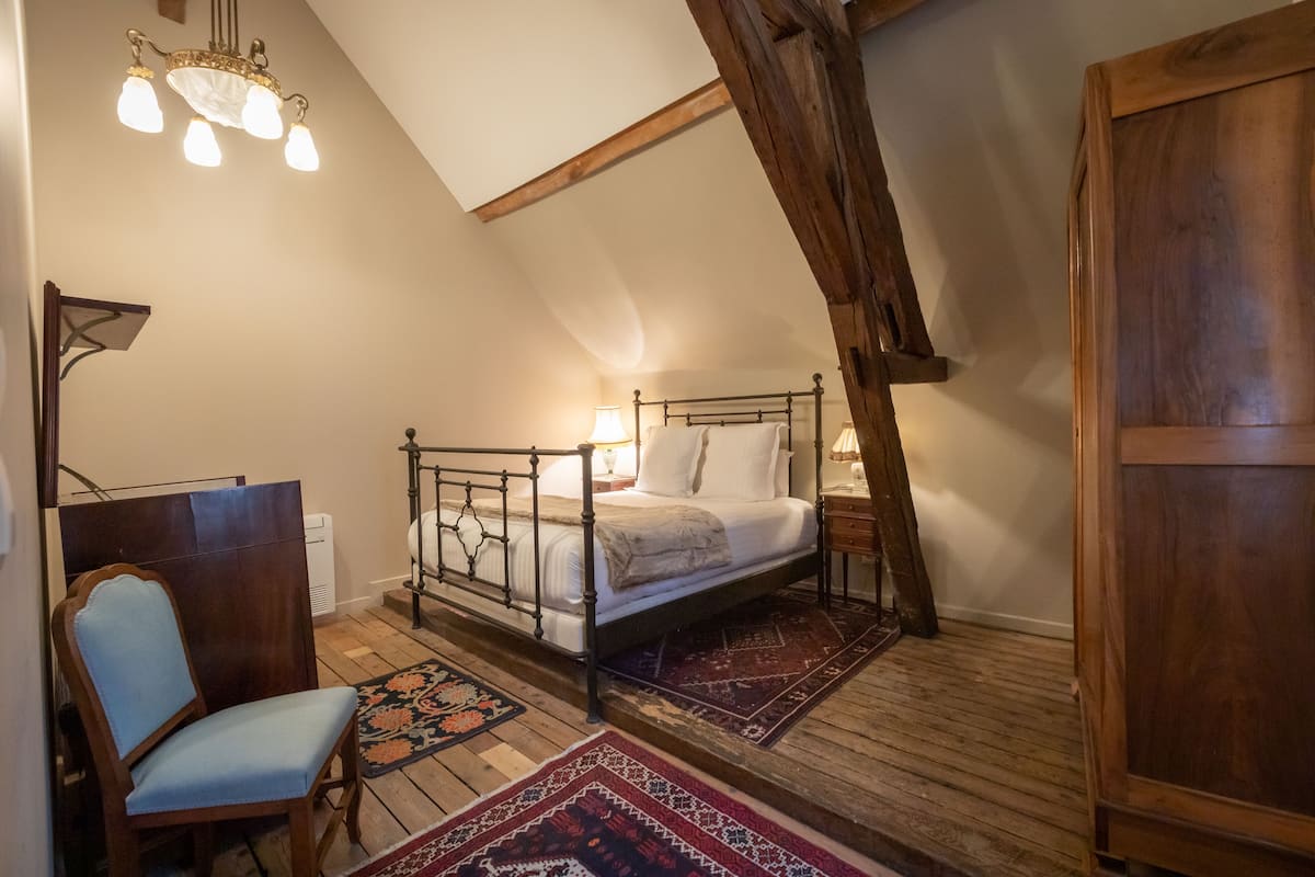 A bedroom with a sloped ceiling, a wooden bed frame, a chair, and a large wardrobe.