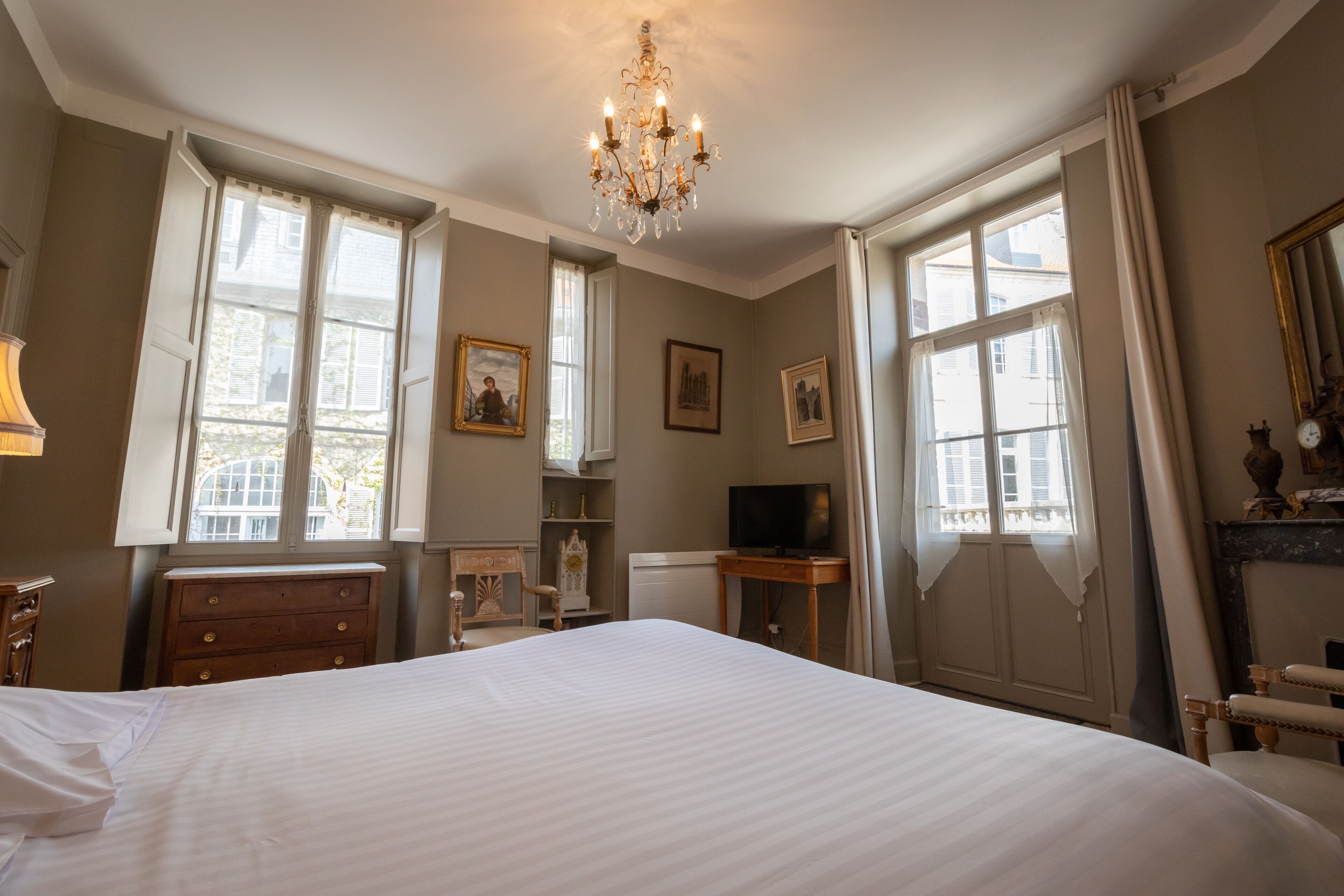 A bedroom with a large bed, a chandelier, a television, and a fireplace.