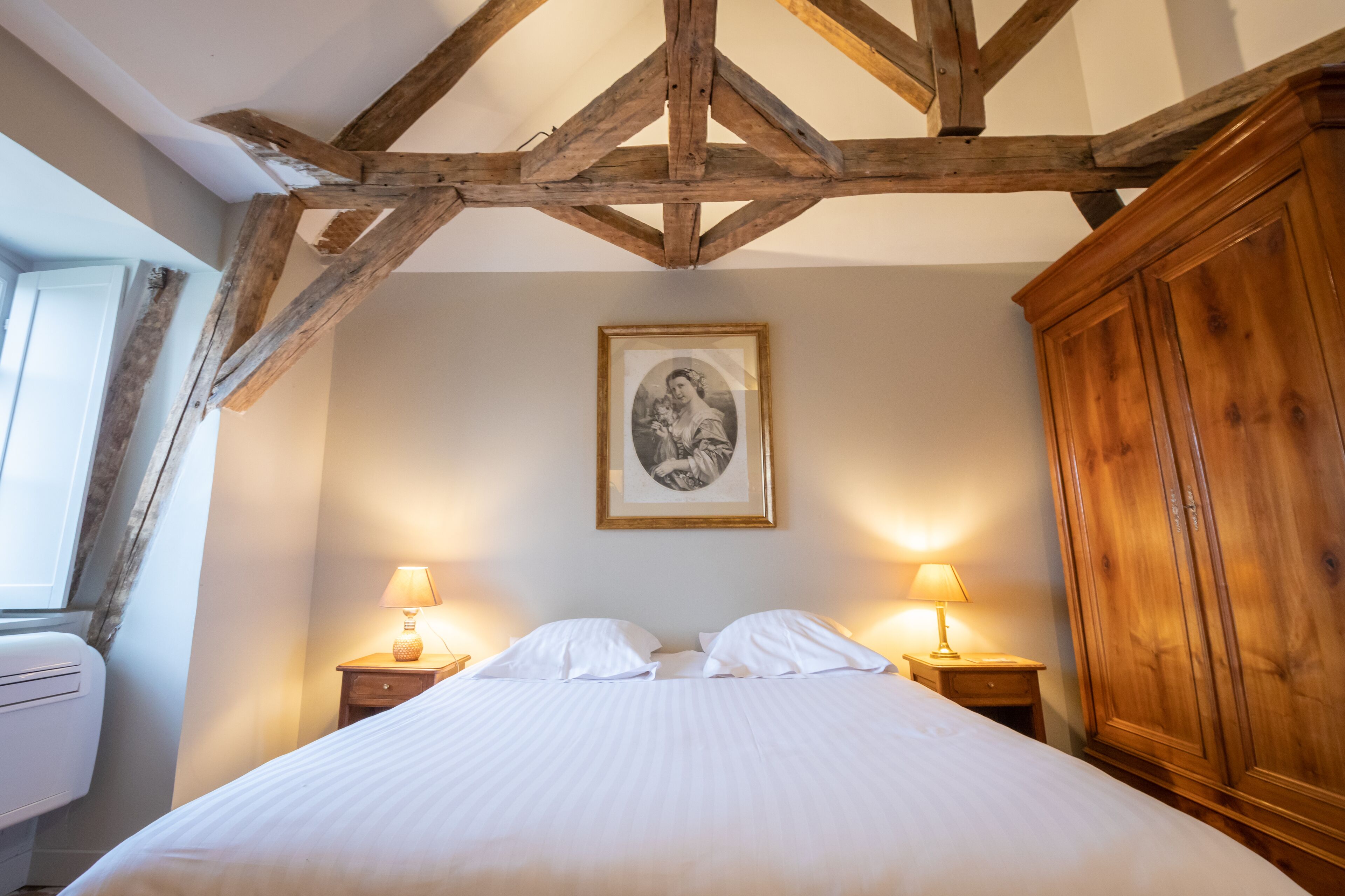 Een slaapkamer met een houten plafond, een bed met witte lakens, twee nachtkastjes met lampen, en een ingelijst schilderij aan de muur.