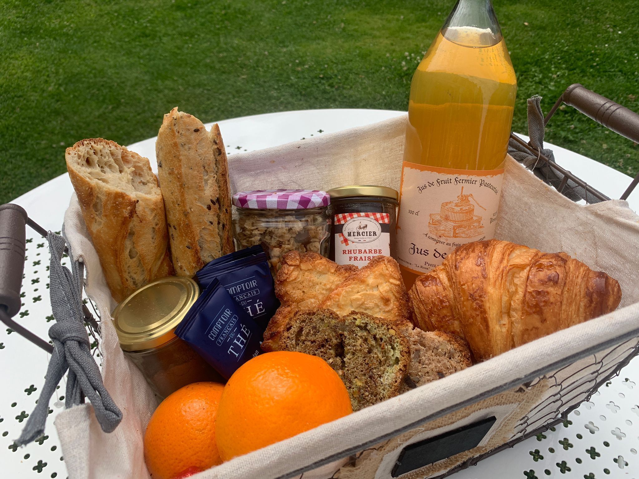 Un cesto da picnic con pane, una bottiglia di succo, un vasetto di marmellata e una brioche su una tovaglia bianca.