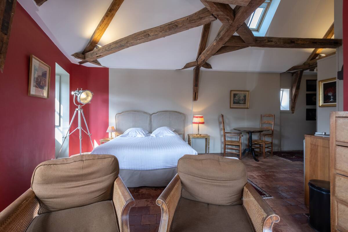 A bedroom with a large bed, wooden beams, a red wall, and a skylight.