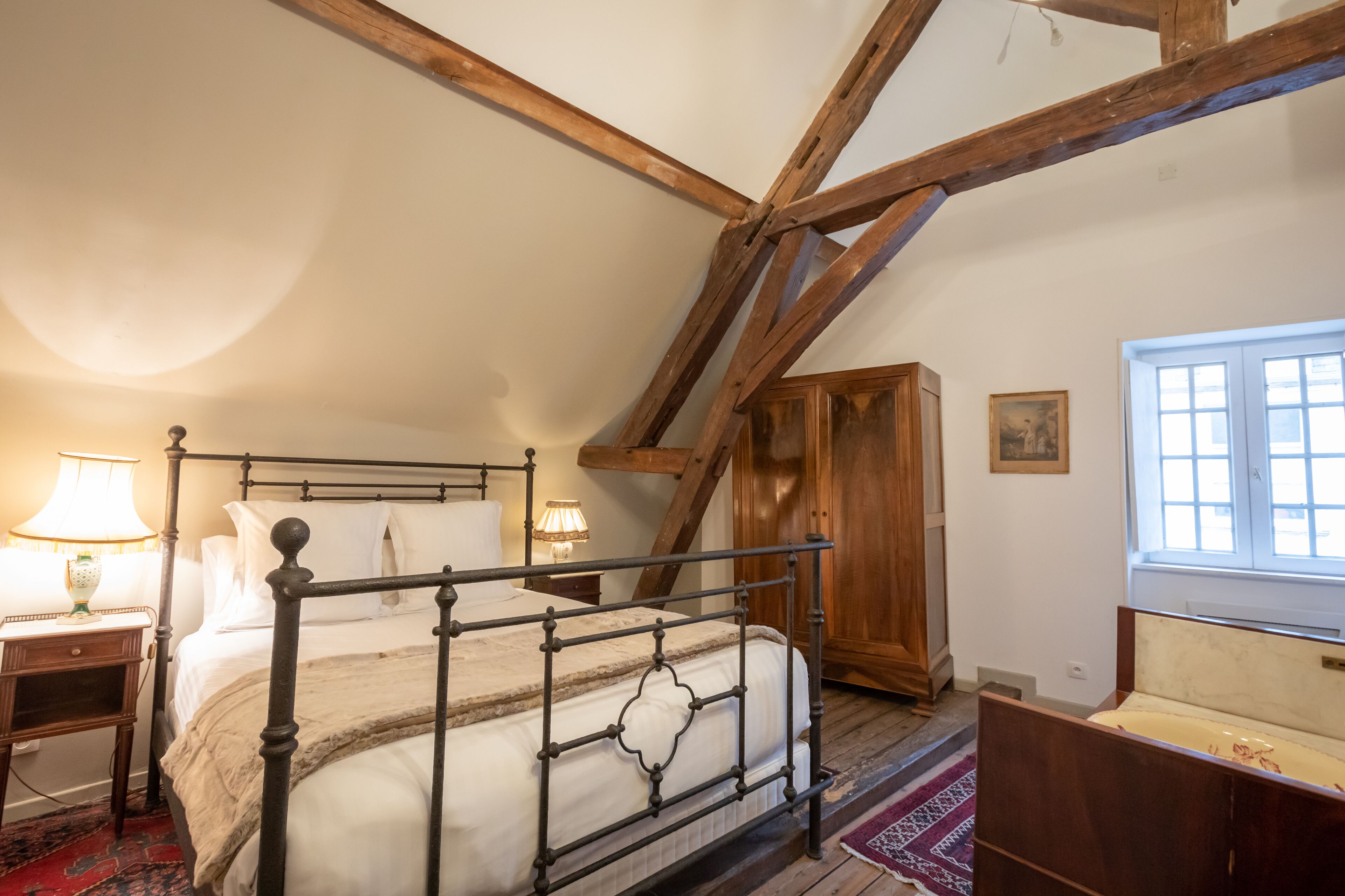 Un dormitorio con cama con dosel, vigas de madera, una ventana y un armario de madera.