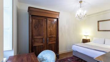 A bedroom with a bed, a wooden wardrobe, a chandelier, a nightstand, and a chair.