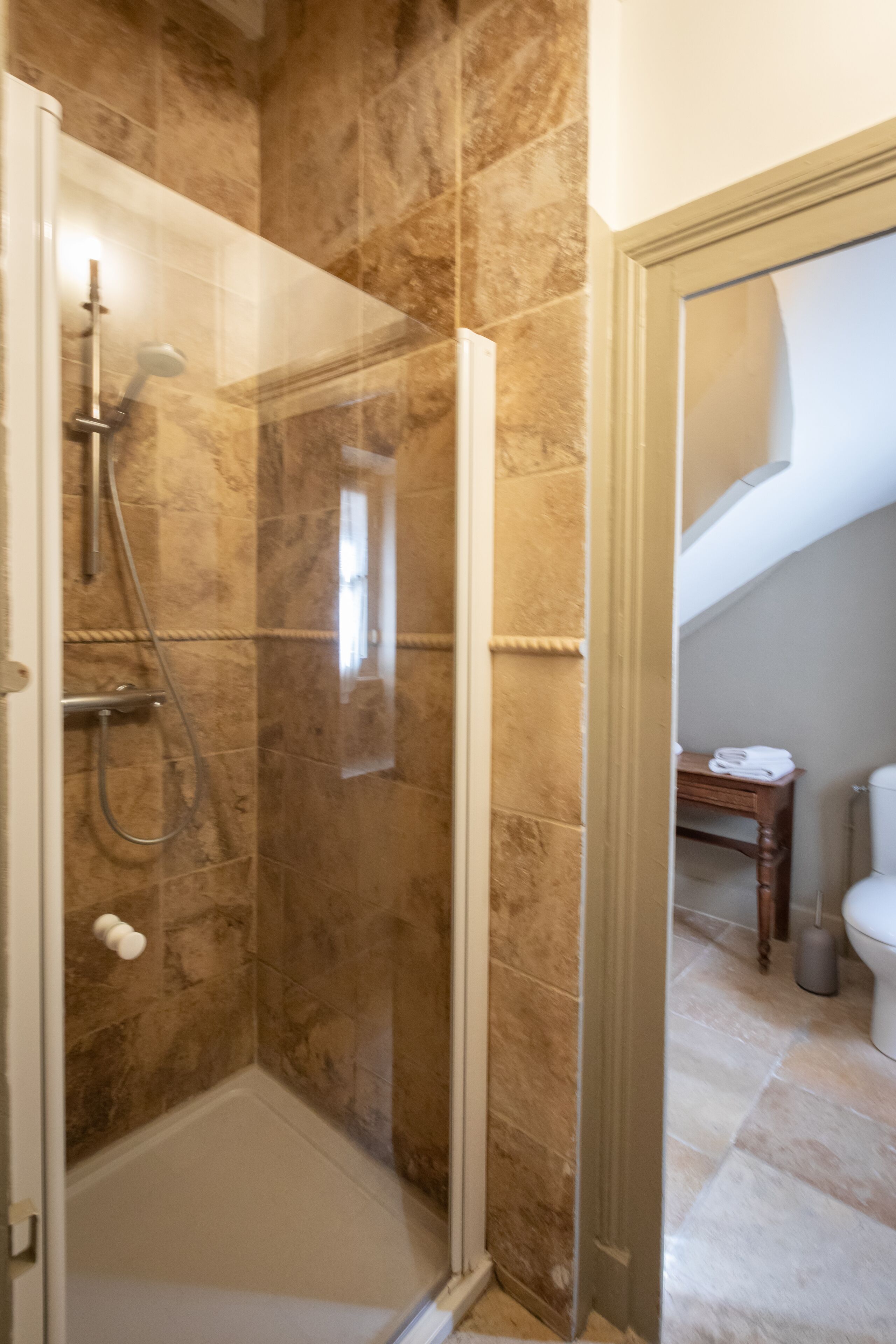 A bathroom with a shower area, a toilet, and a small table with towels.