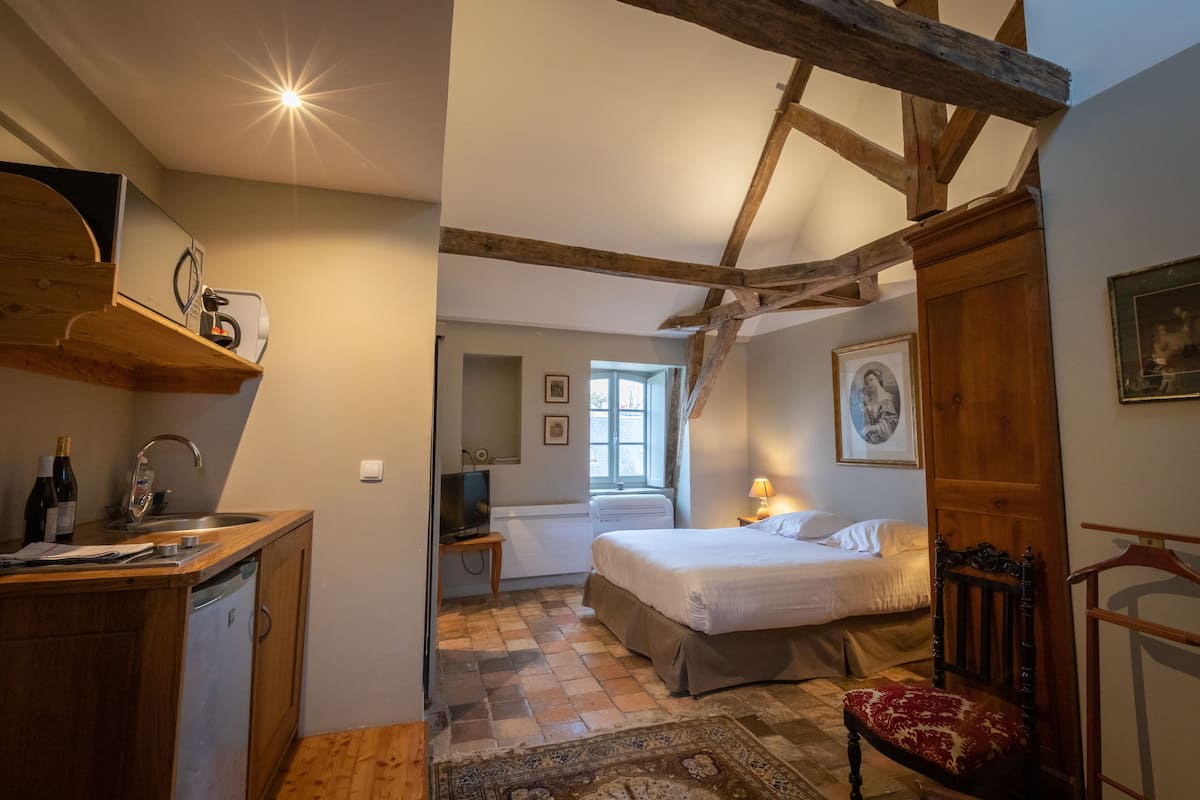 A bedroom with a bed, a chair, a desk with a sink, and a window.