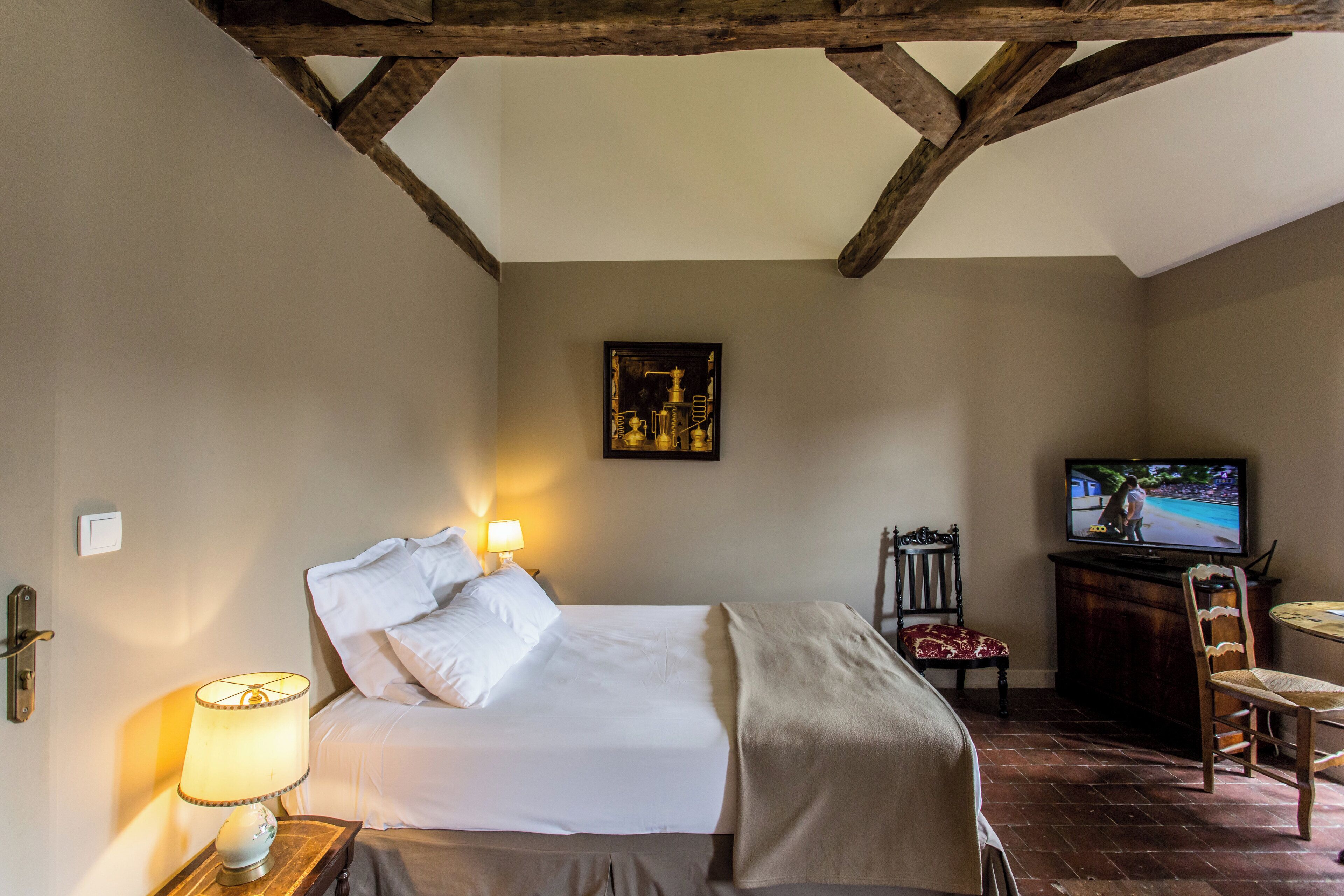A bedroom with a bed, bedside lamp, TV, and a chair.