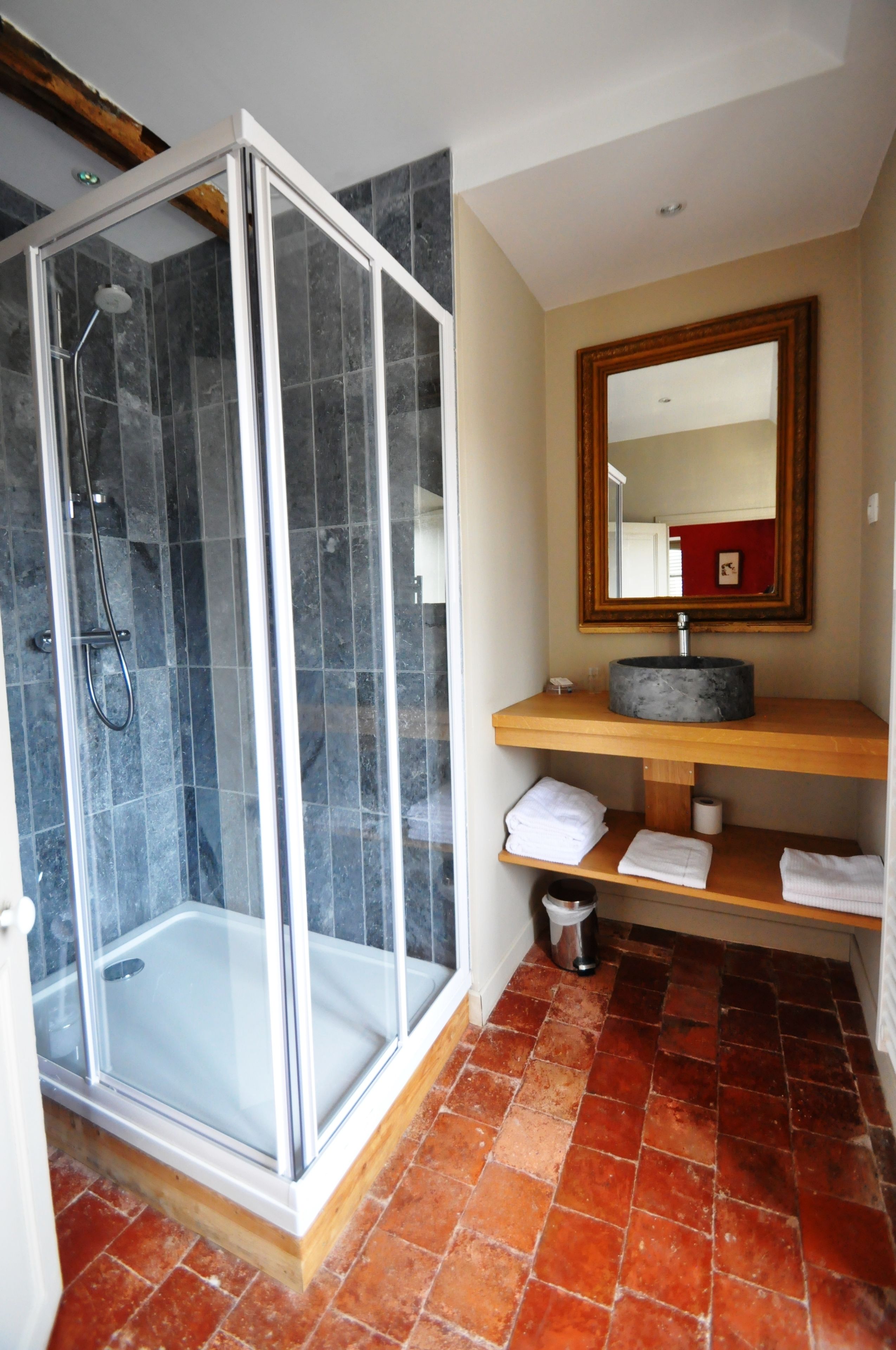 Ein modernes Badezimmer mit einer gläsernen Dusche, einem Holzkosmetikschrank mit rundem Waschbecken und einem Spiegel darüber.