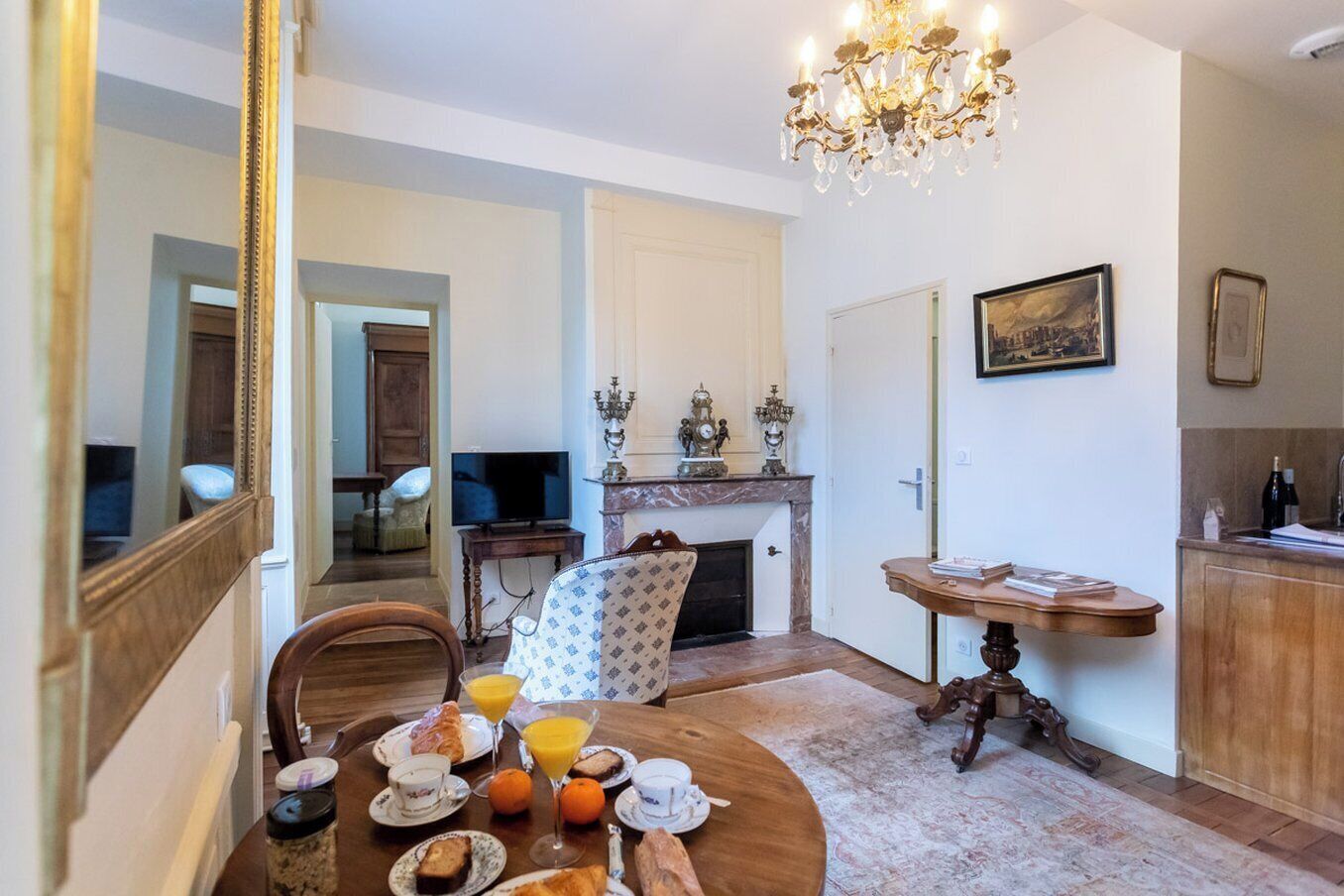 A dining area with a round table set for breakfast, a television, a fireplace, and a chandelier.