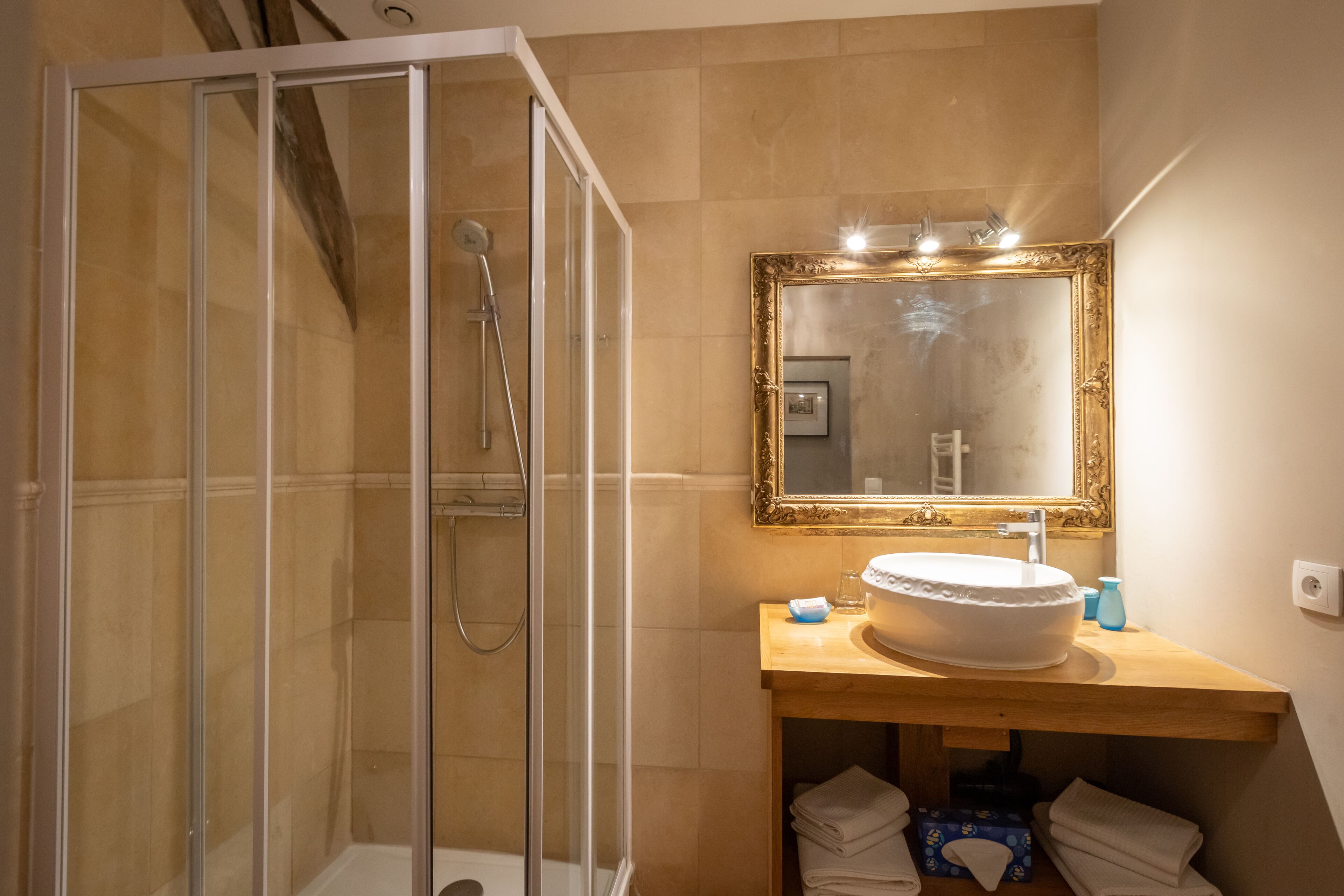 Un baño con ducha acristalada, tocador de madera con lavamanos y un espejo grande encima.