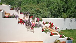 A white building with multiple levels, each adorned with flower boxes containing red and pink flowers. - Aptera Paradise (Chania)