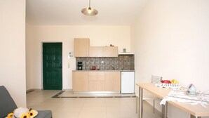 A compact kitchen with a green door, a coffee machine, and a dining area with a table set for two. - Aptera Paradise (Chania)