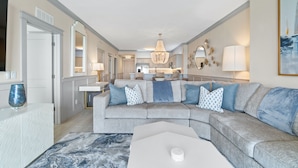 A modern living room with a grey sectional sofa, a white coffee table, and a chandelier. - Tropic Winds by Panhandle Getaways (Panama City Beach)