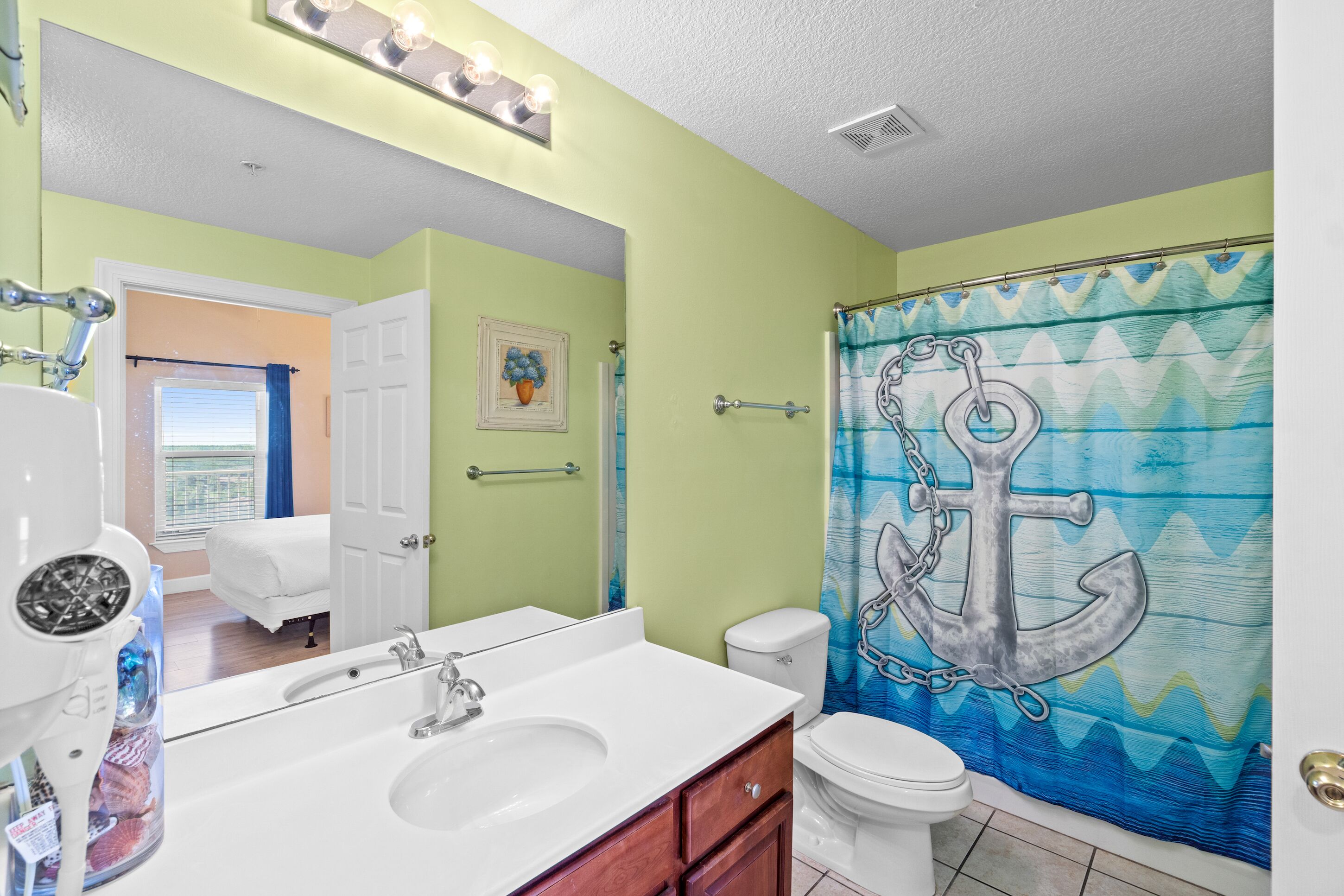 Une salle de bain avec un lavabo blanc, des toilettes et un rideau de douche orné d’un motif d’ancre.