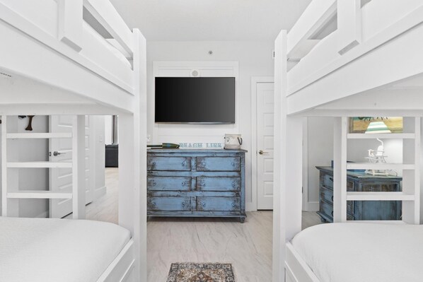 A bedroom with bunk beds, a television, a dresser, and a desk.
