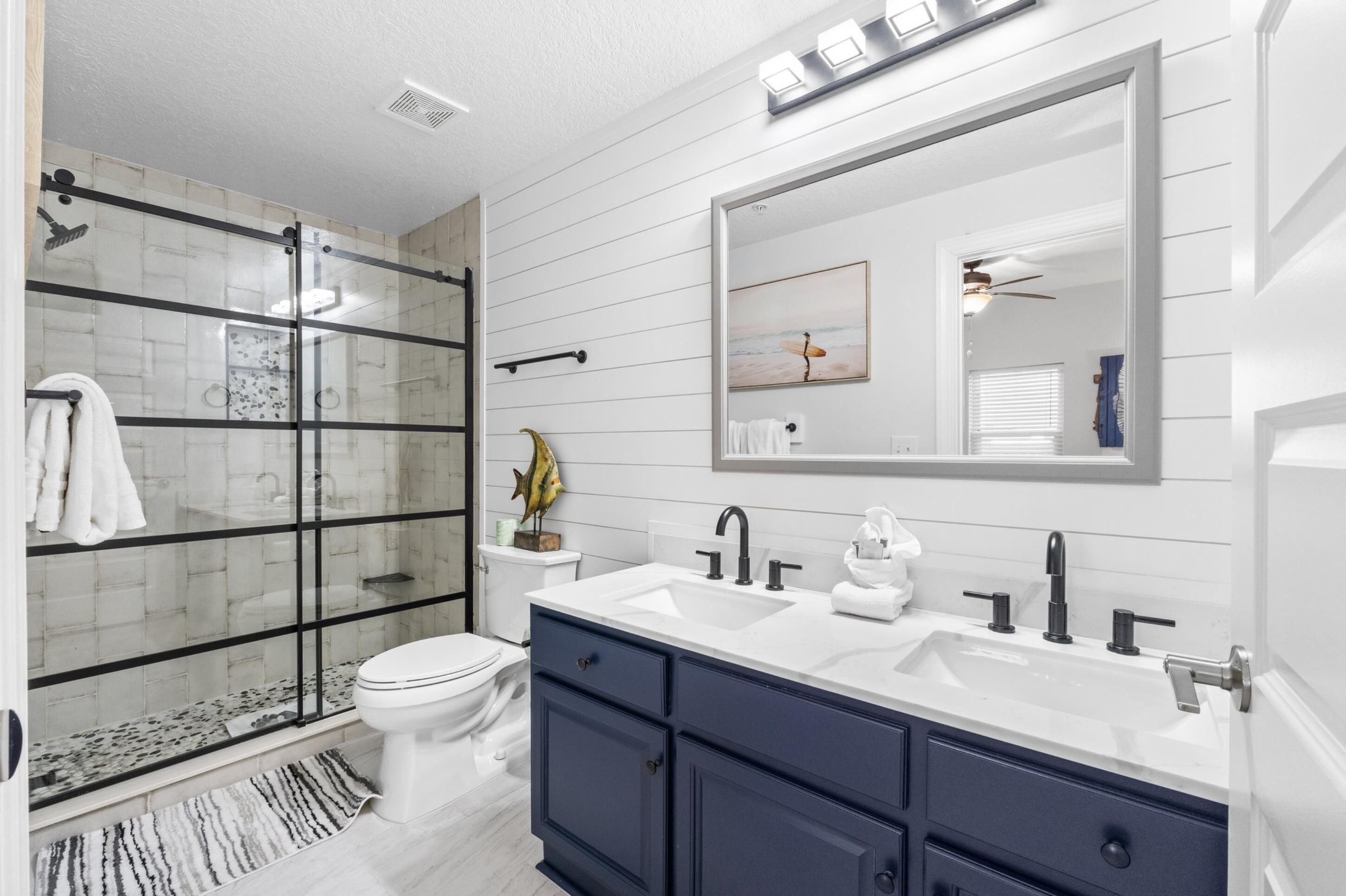 A modern bathroom with a glass-enclosed shower, a white toilet, a double sink vanity, and a large mirror.