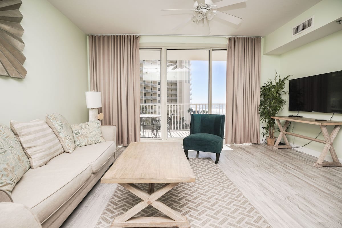 A modern living room with a sofa, a coffee table, a TV, and a balcony with curtains.
