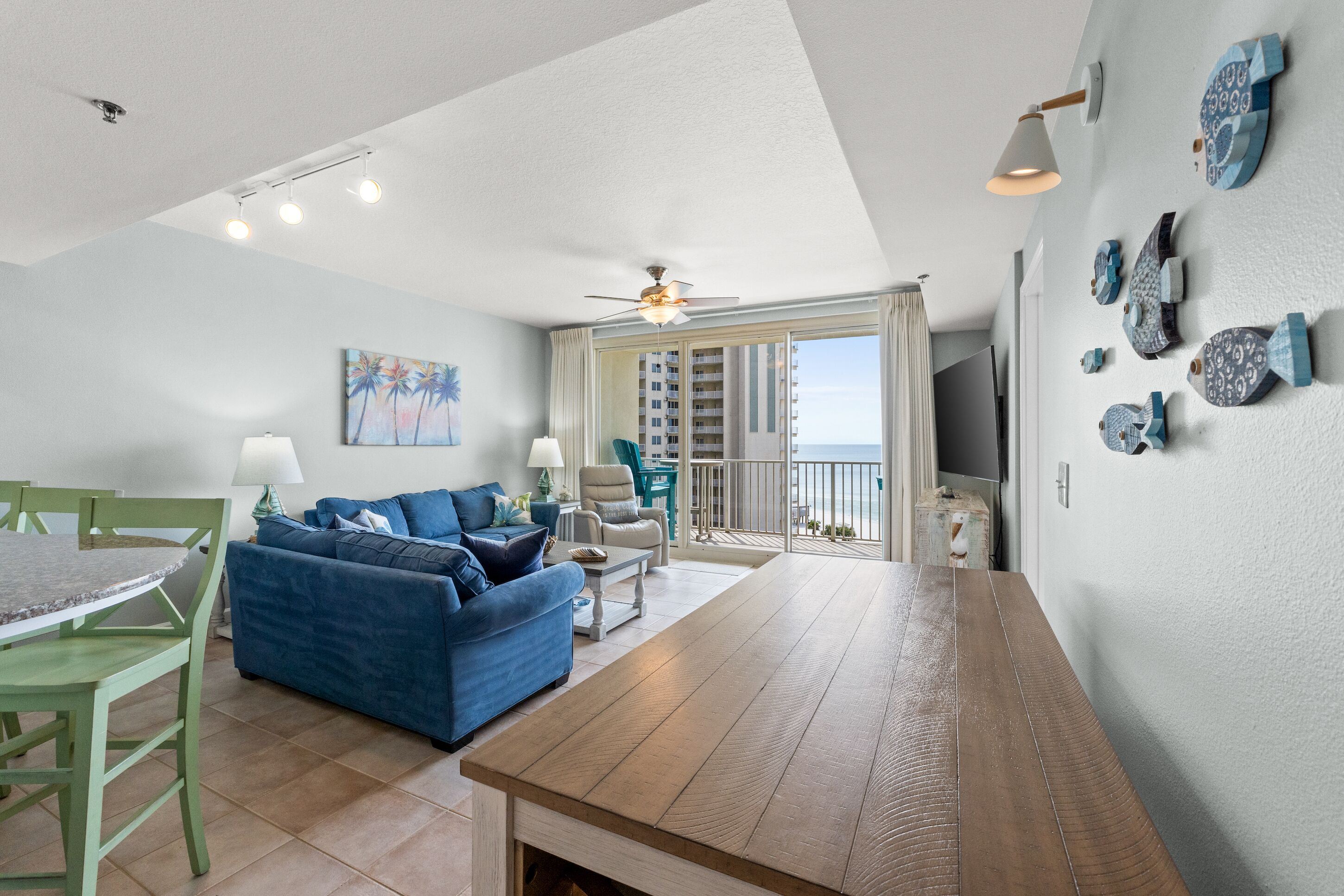 A living room with a wooden table, blue sofa, and a view of the ocean through large windows.