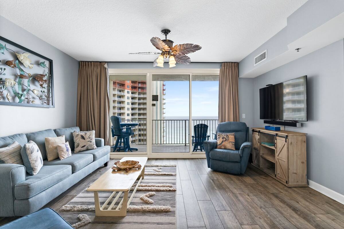 A modern living room with a sofa, armchair, coffee table, and a ceiling fan.