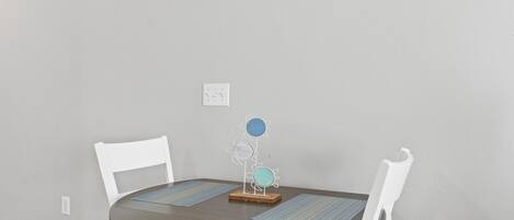 A round dining table with two white chairs, a decorative metal flower stand, and two placemats.