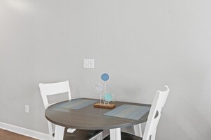 A round dining table with two white chairs, a decorative metal flower stand, and two placemats.
